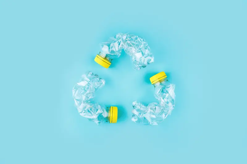 Three crashed plastic bottles on blue background form recycling sign