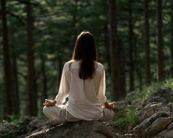 Woman meditating on rock in forest